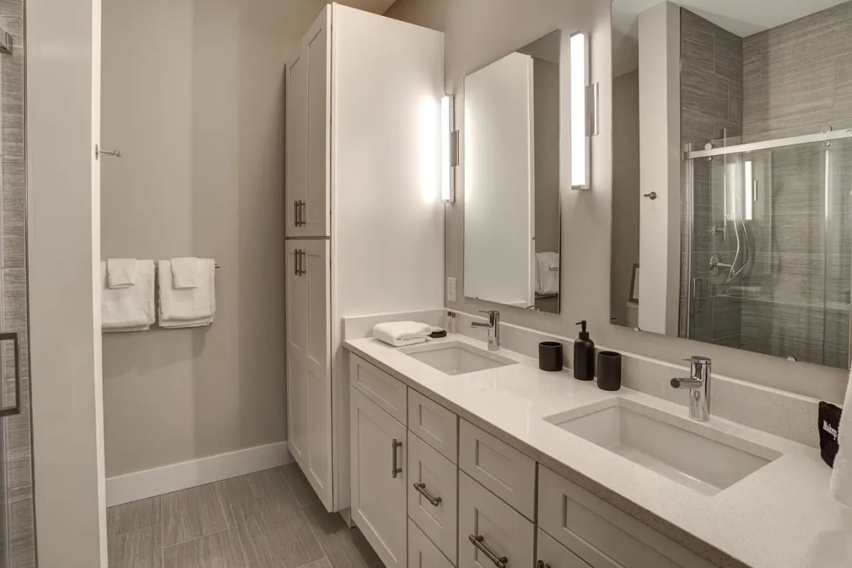 A bright, modern bathroom featuring double vanity sinks, large mirrors, and stylish fixtures. The spacious layout and tranquil mood invite guests to enjoy moments of self-care and relaxation.