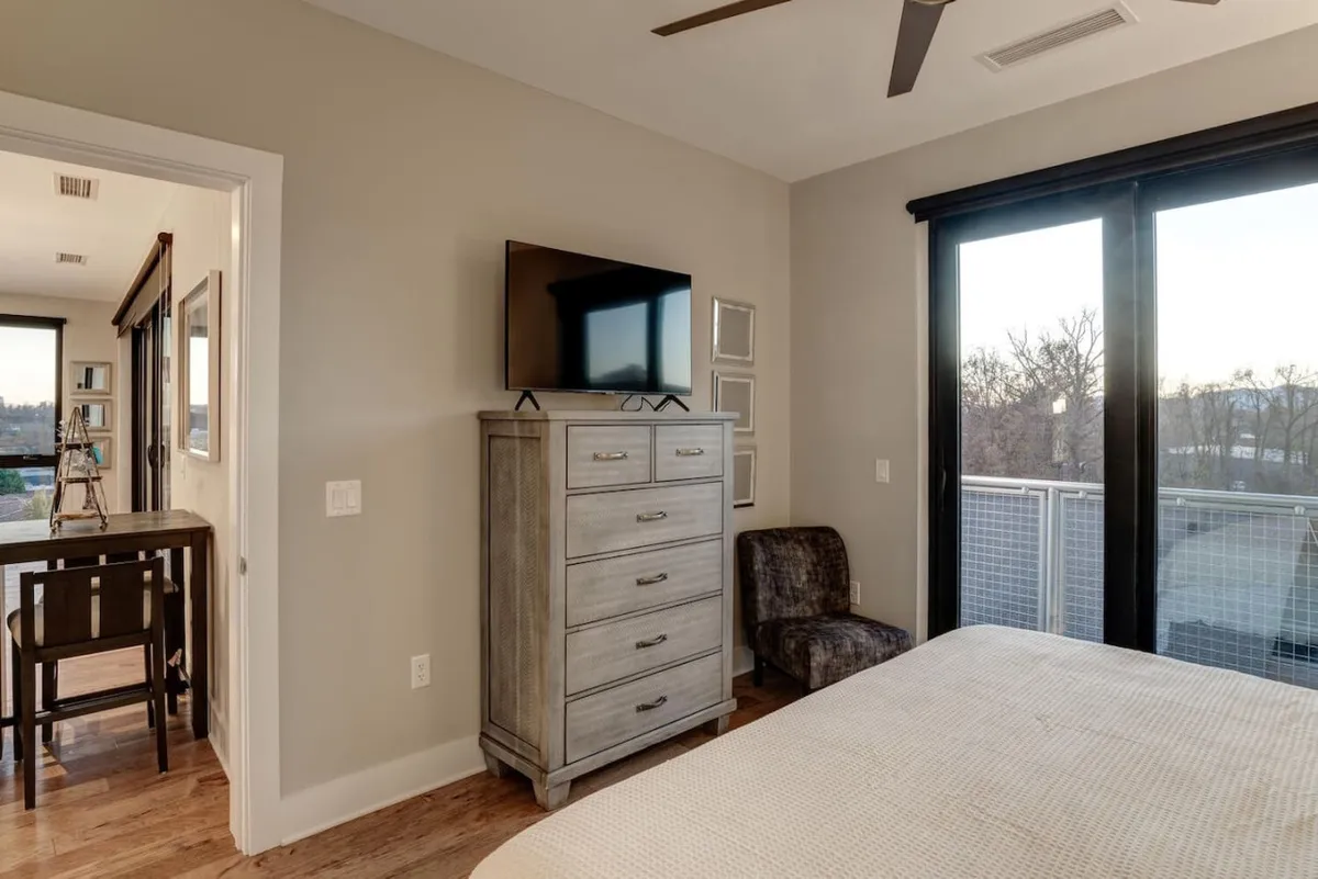 A tranquil bedroom scene with a bed, armchair, dresser, and a balcony door. The setup allows clear sightlines from the bed and chair out to the balcony, suggesting easy access to inspiring views and natural light.