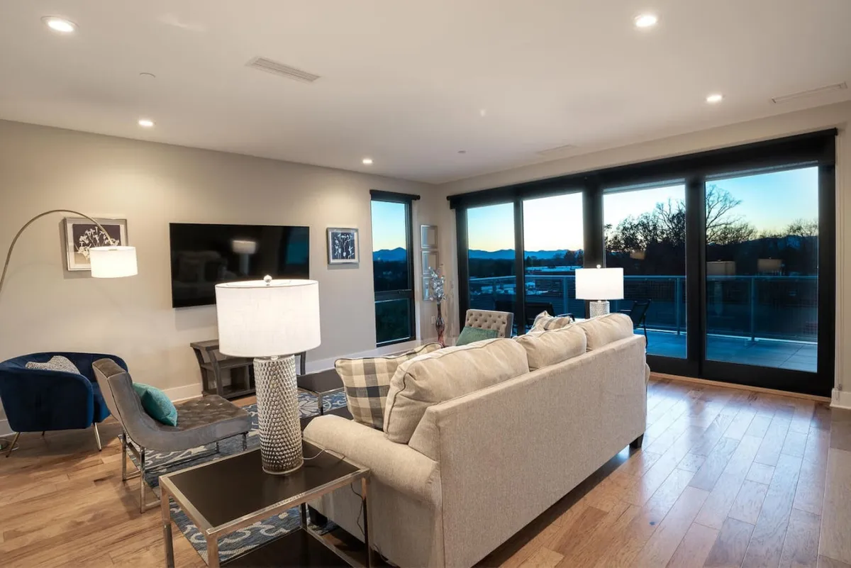 A cozy yet sophisticated living space with a large, plush sofa positioned to take in the expansive sunset view through oversized windows. A stylish coffee table and decorative lamp complete the scene, suggesting a refined atmosphere ideal for both relaxation and entertaining.