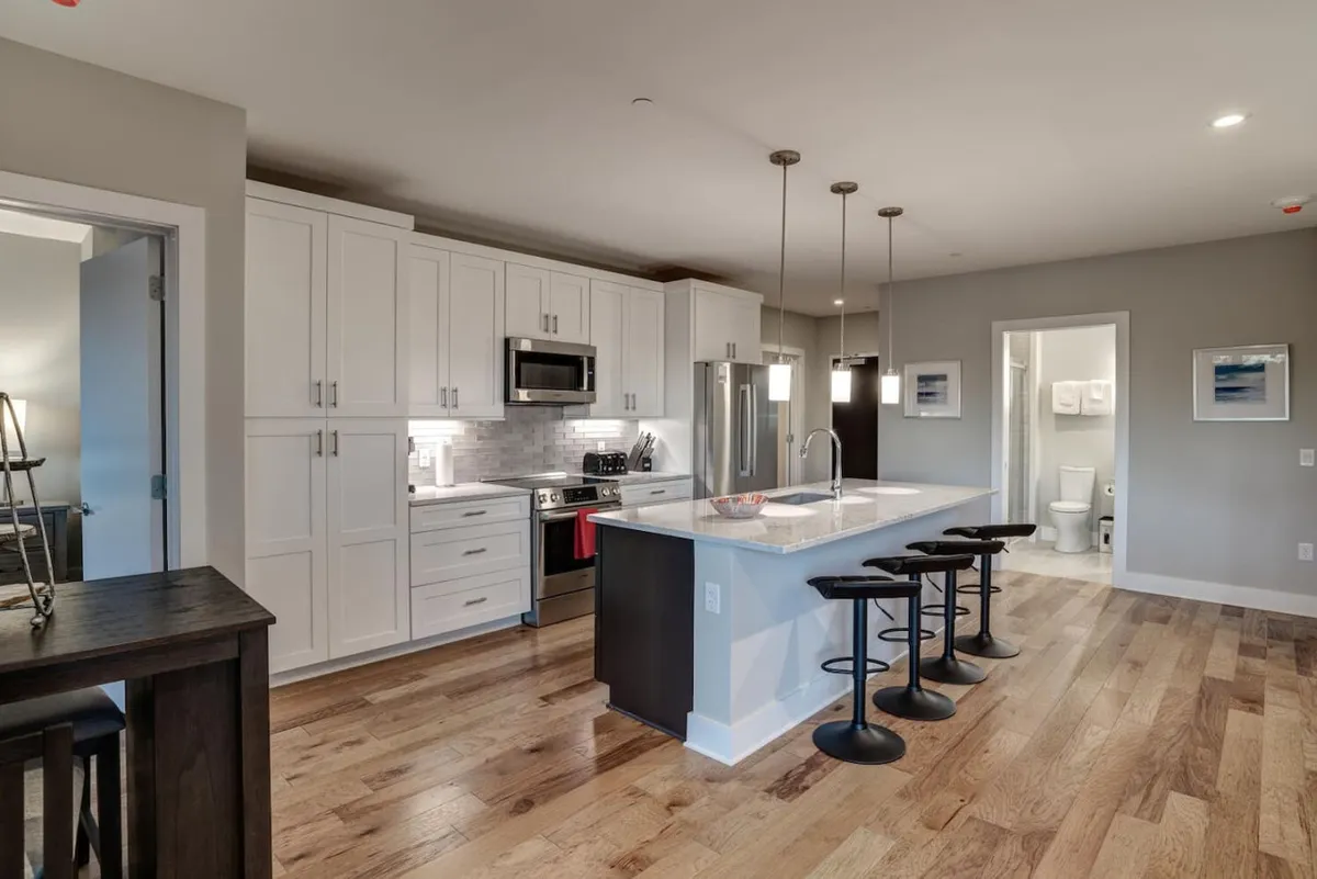 Another angle of the kitchen, highlighting the large island, multiple bar stools, stainless steel appliances, and elegant cabinetry. The atmosphere is modern and inviting, suggesting a space built for entertaining and memorable meals.