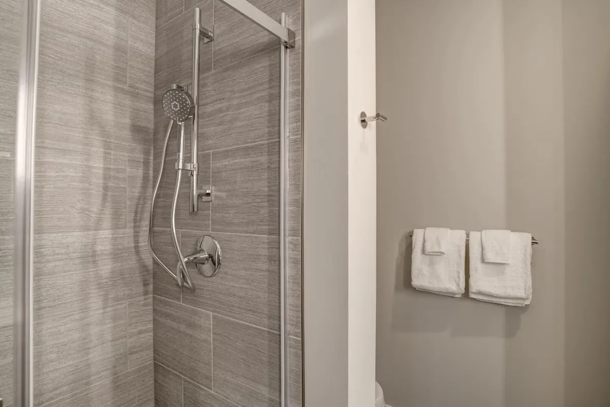 A modern shower area with sleek gray tiles and fresh towels neatly arranged, exuding a sense of cleanliness and comfort. The design is contemporary and spa-like, ideal for unwinding after a busy day or refreshing in the morning.