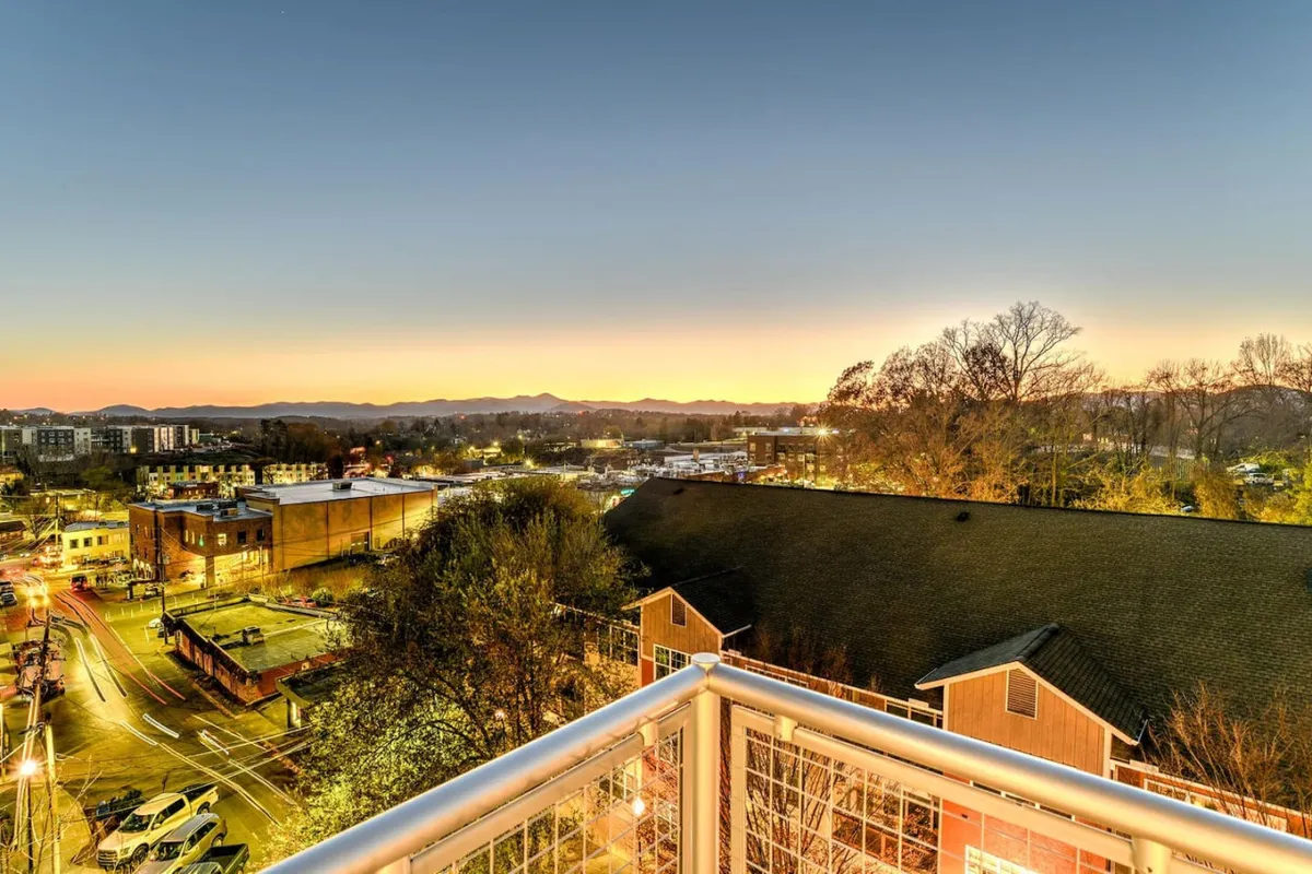 A sweeping view of the urban skyline transitions into a majestic mountain range under a sunset sky. The tranquil mood captures the peaceful coexistence of city life and nature.