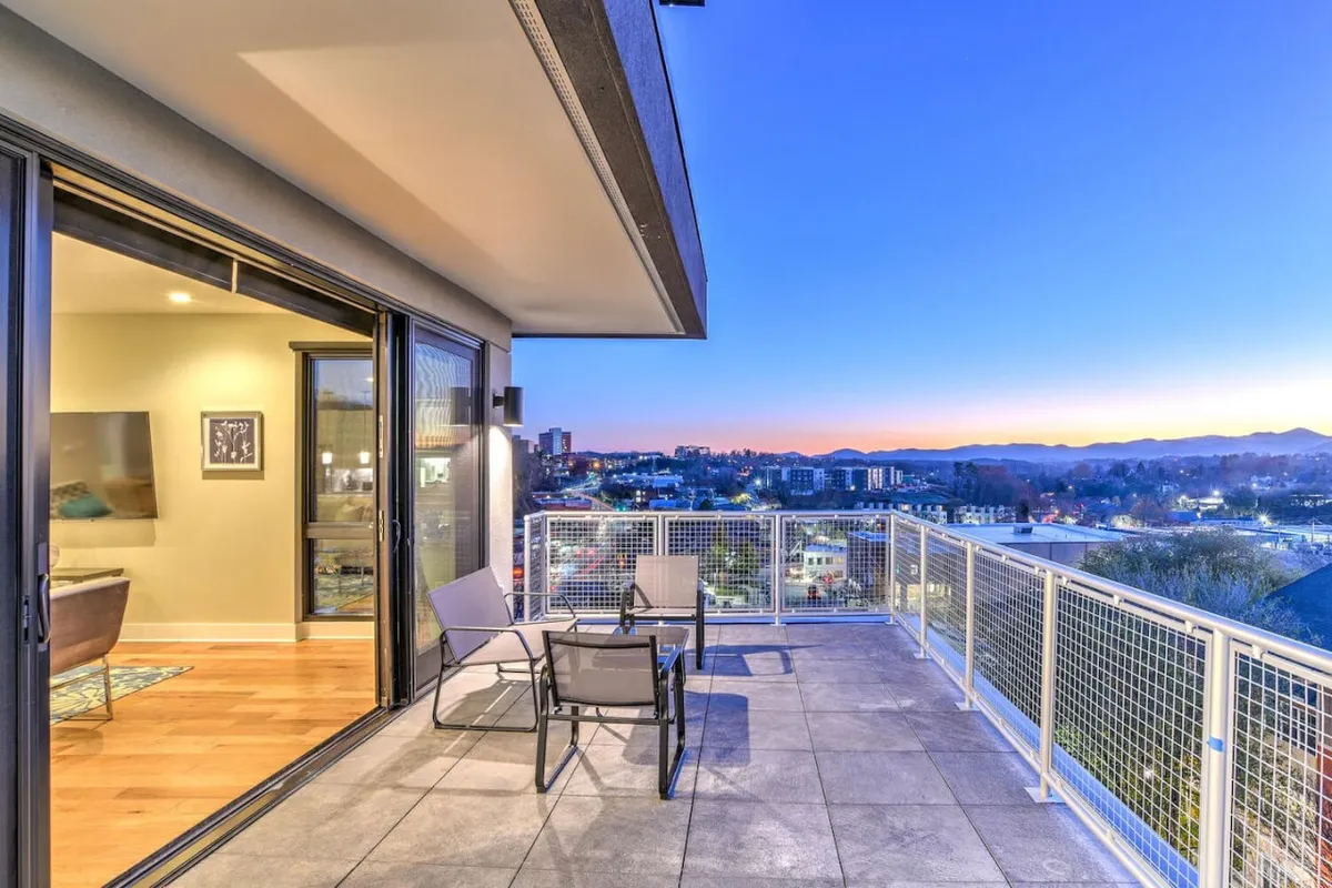 An exterior patio with comfortable seating overlooks the cityscape, with a dramatic mountain backdrop visible in the distance. The serene setting suggests an ideal place to unwind after a day of exploring the city.