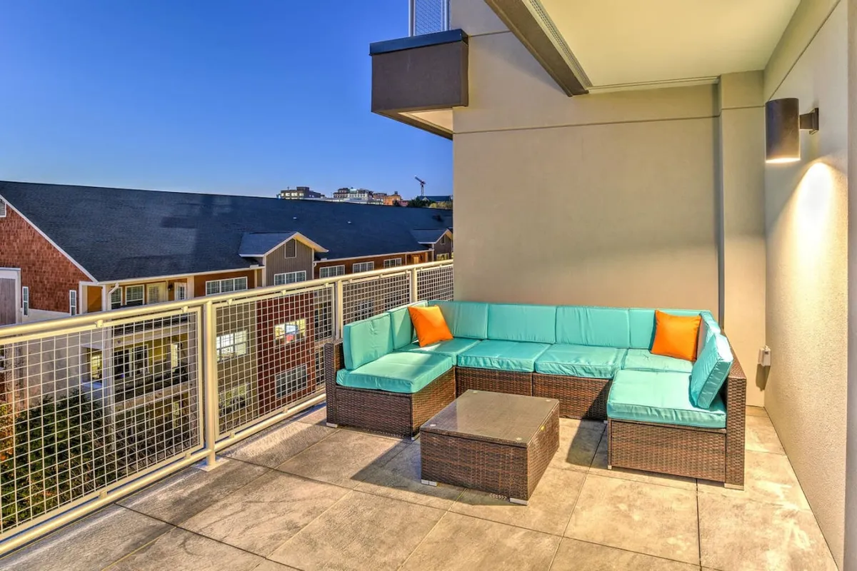 A tranquil exterior shot of a balcony lounge setup, featuring an L-shaped couch, coffee table, and the balcony railing. This inviting space is perfect for relaxing after exploring Asheville’s breweries or music venues. The setting suggests both stargazing and socializing under the night sky.