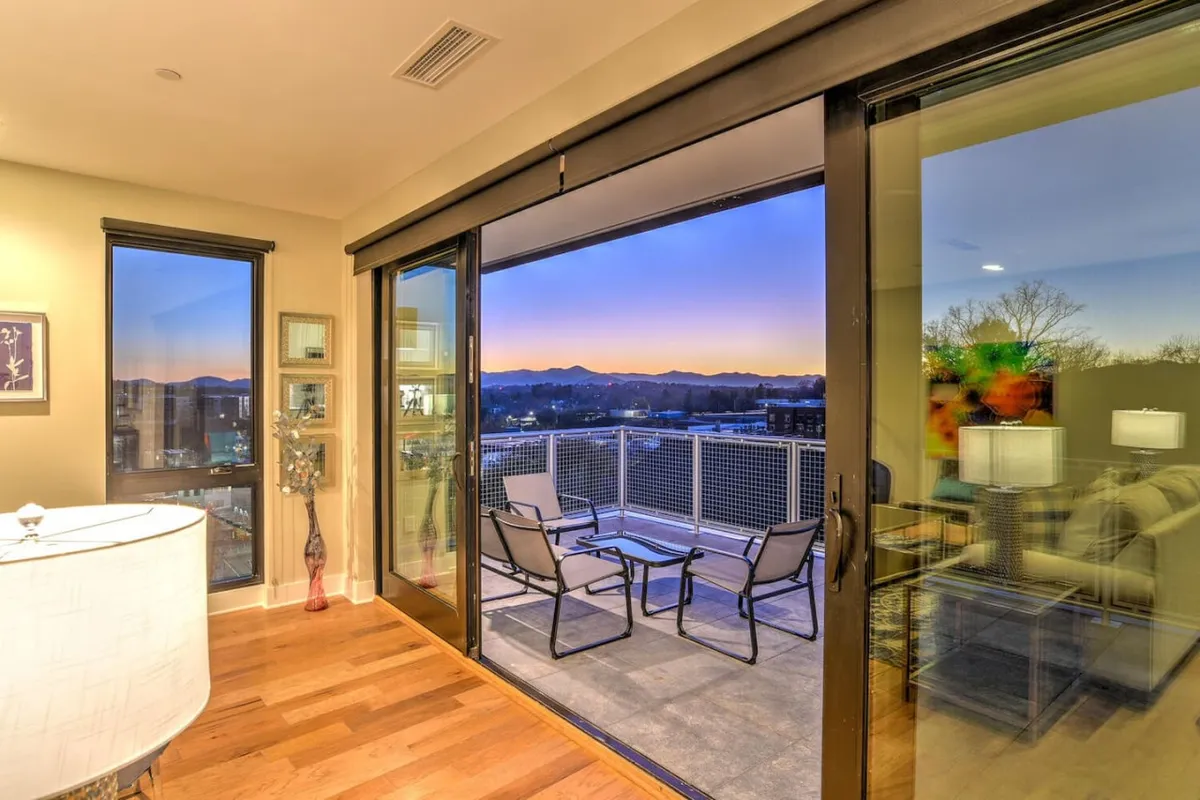 This image features a cozy, modern living space with sliding glass doors that open onto an outdoor seating area. The scene is calm and inviting, with decorative accents and a focus on the indoor-outdoor connection. The balcony beyond the glass doors hints at mountain views and sunset gatherings mentioned in the section.