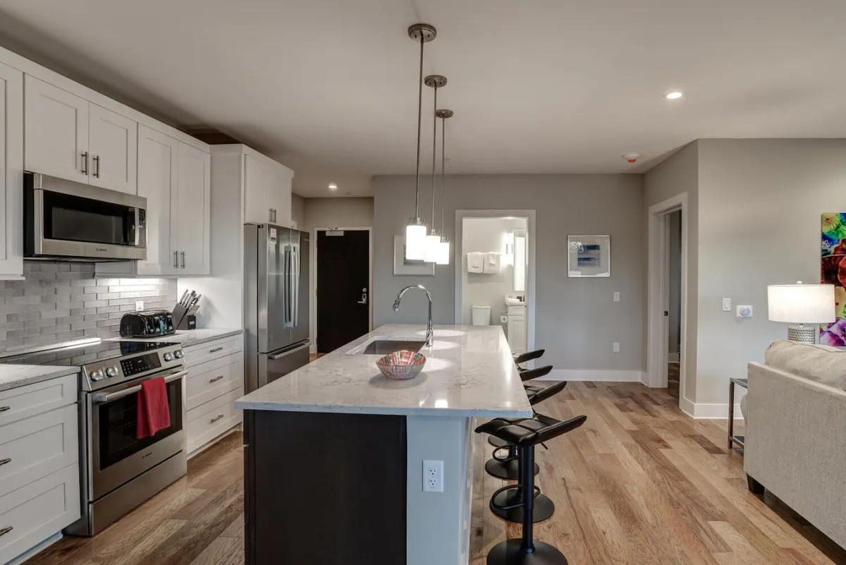 A modern kitchen with a prominent island, premium stainless steel appliances, stylish pendant lighting, and bar stools. The setting is open and inviting, ideal for both cooking and socializing.